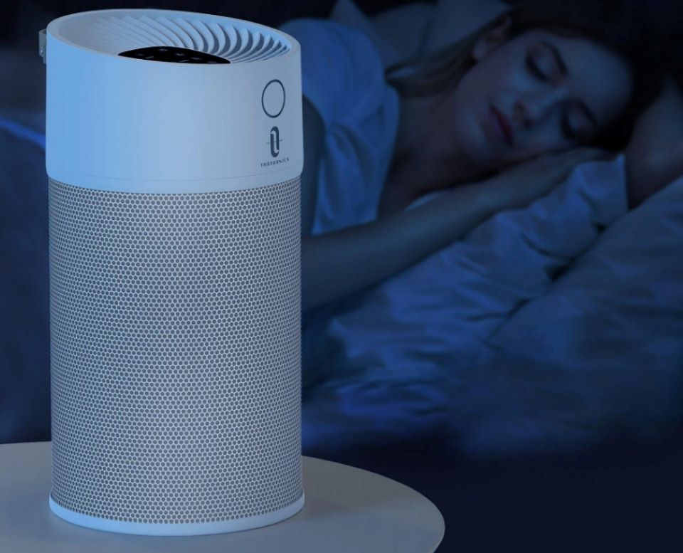Air purifier on a nightstand with a woman sleeping in the background
