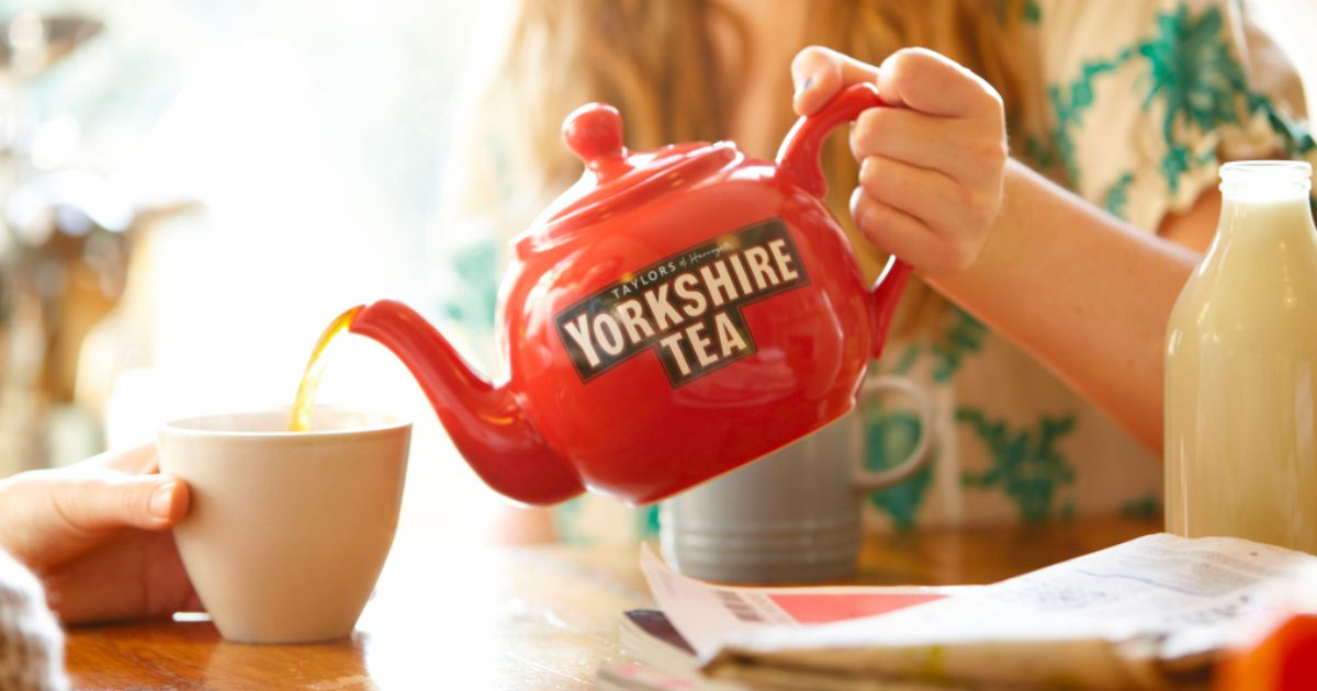 a womans hand pouring a cup of Taylors yorkshire tea out of a red tea pot 