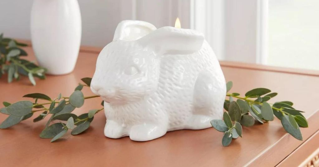 Candle shaped like a bunny on a table with faux greenery around it