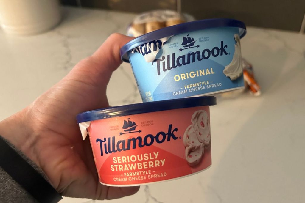 a womans hand holding two 7 ounce containers of Tillamook cream cheese 