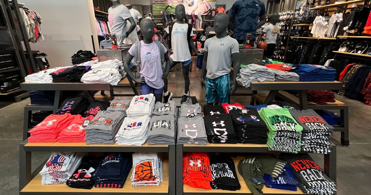 Under Armour Kids clothing display in-store with folded shirts and child mannequins wearing Under Armour Clothing