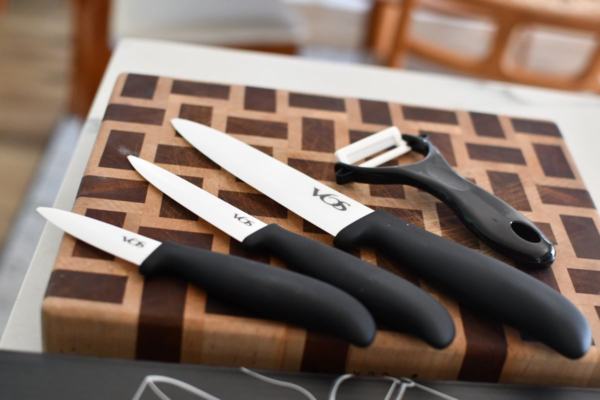 Three knives with black handles, and a vegetable peeler on a cutting board.