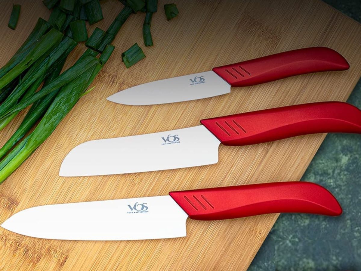 Three knives with white blades and red handles on a cutting board