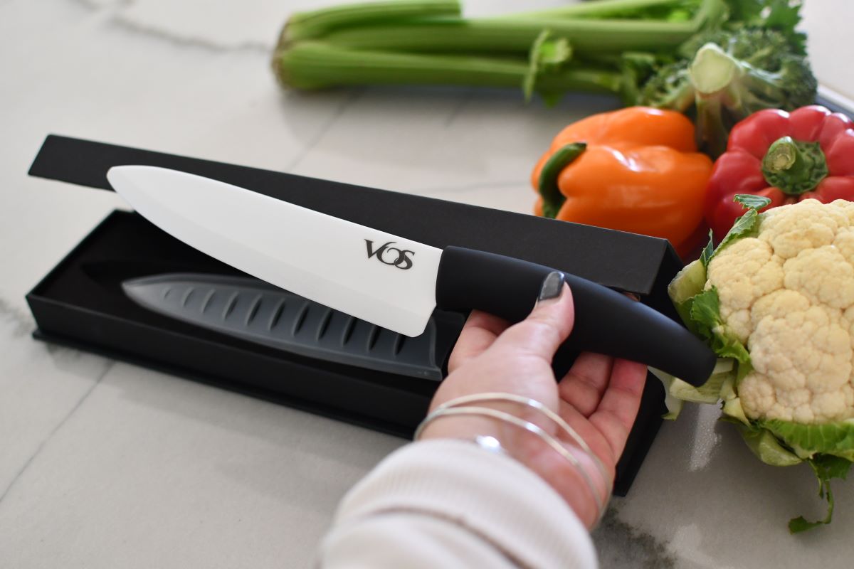 Hand holding a chef's knife next to the box with vegetables near the box