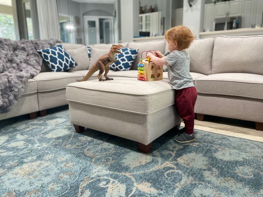 Boy standing next to an ottoman playing with toys