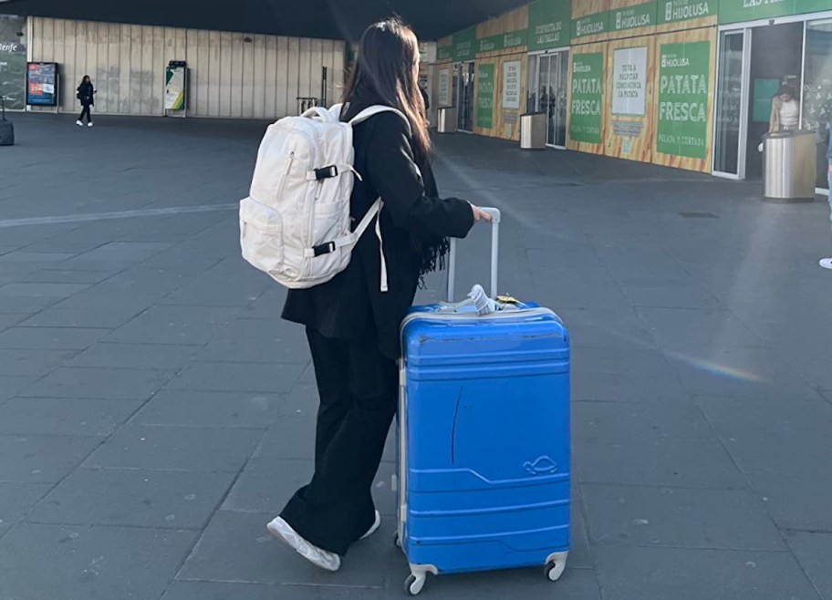 woman standing with blue suitcase and white travel backpack