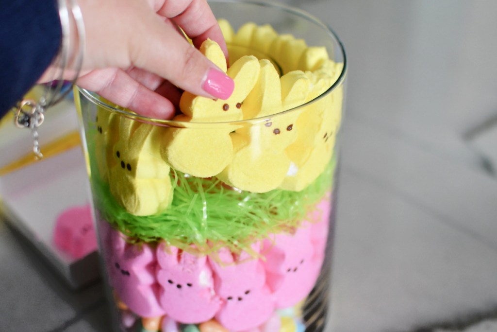 adding faux grass and yellow peeps to a glass vase centerpiece