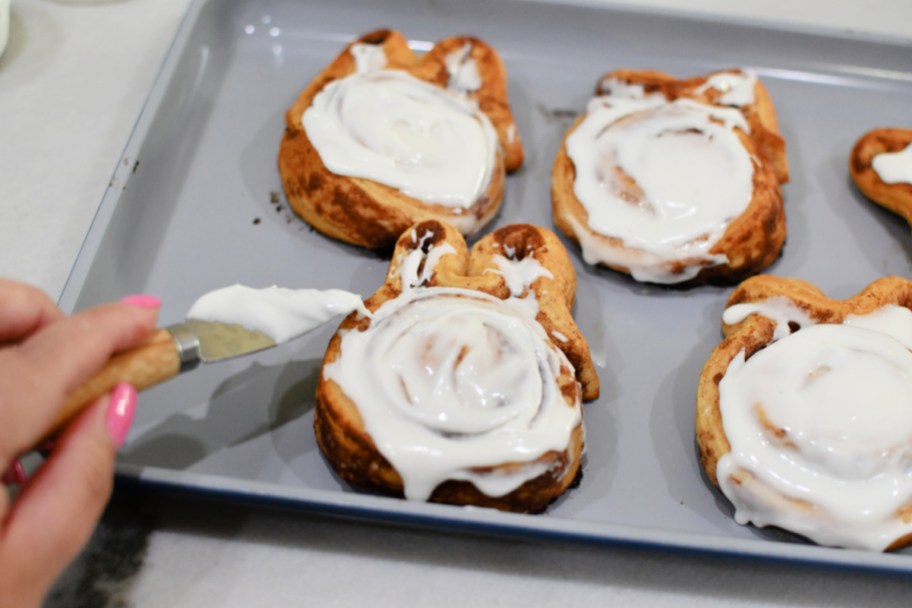 adding frosting to easter bunny cinnamon rolls after baking
