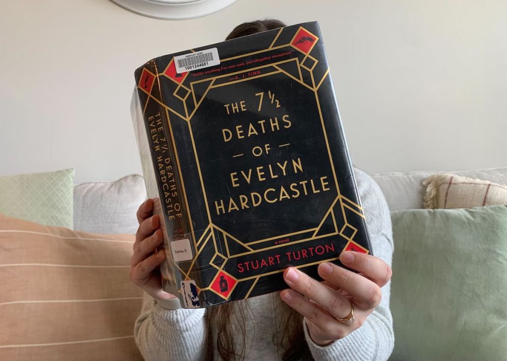 woman holding the 7 1/2 deaths of evelyn hardcastle book