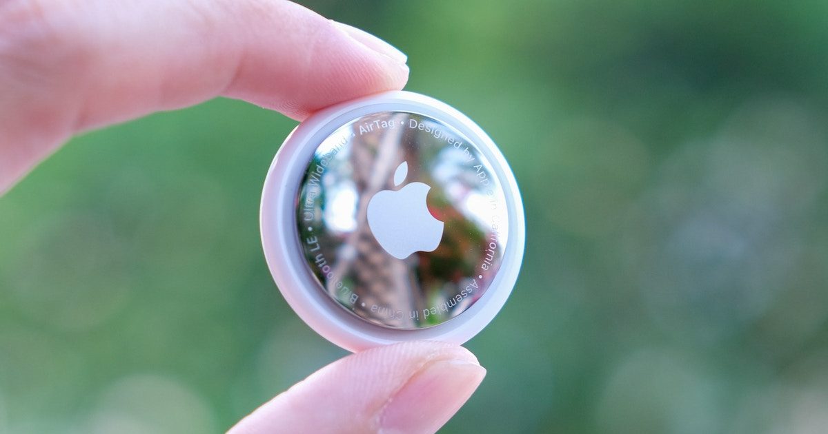 close up of fingers holding apple airtag in front of greenery