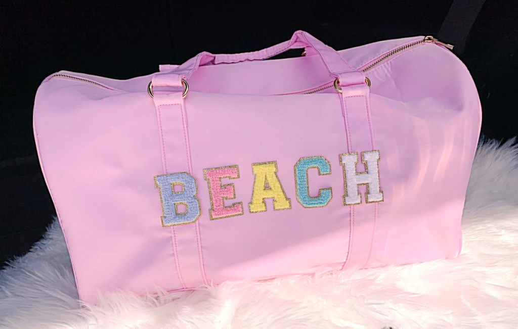 pink duffle bag with pink patches spelling beach on front