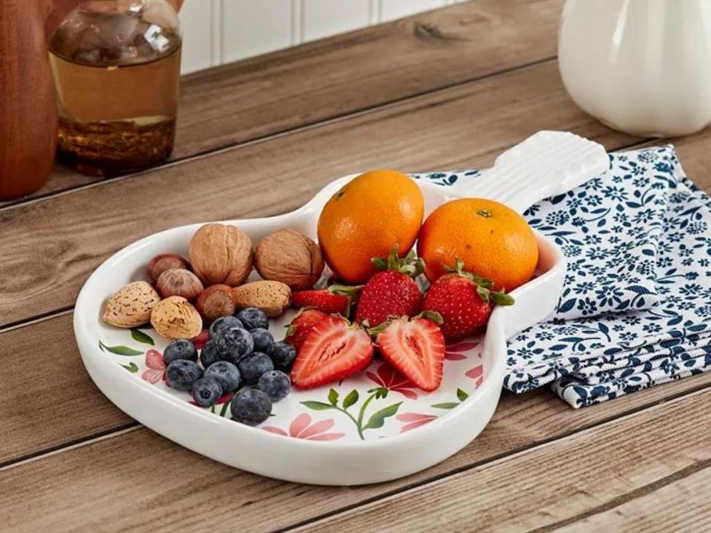 floral white ceramic guitar serving tray with oranges, walnuts, blueberries, and strawberries on it.