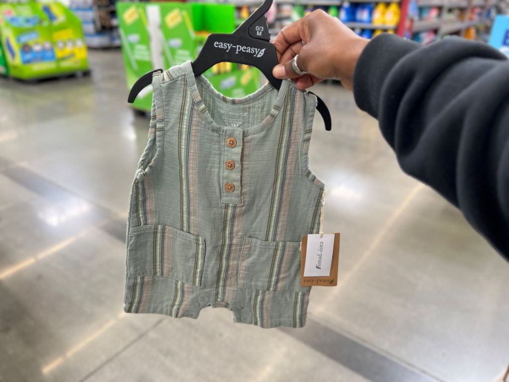 Hand holding a green triped romper on a hanger