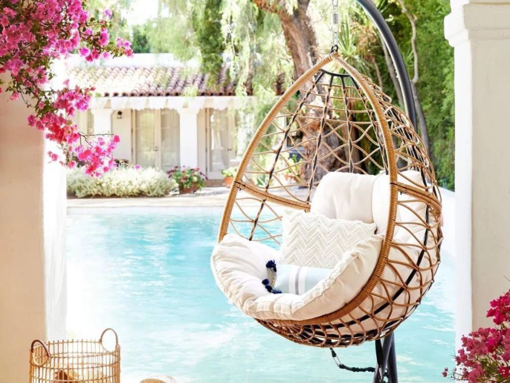 wicker hanging egg chair with white cushion on patio by pool