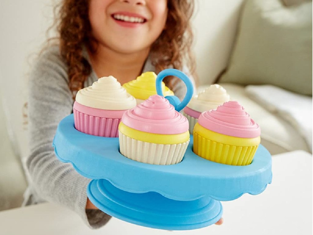 girl showing Green Toys Cupcake 16-Piece Set in blue with pink and white cupcakes