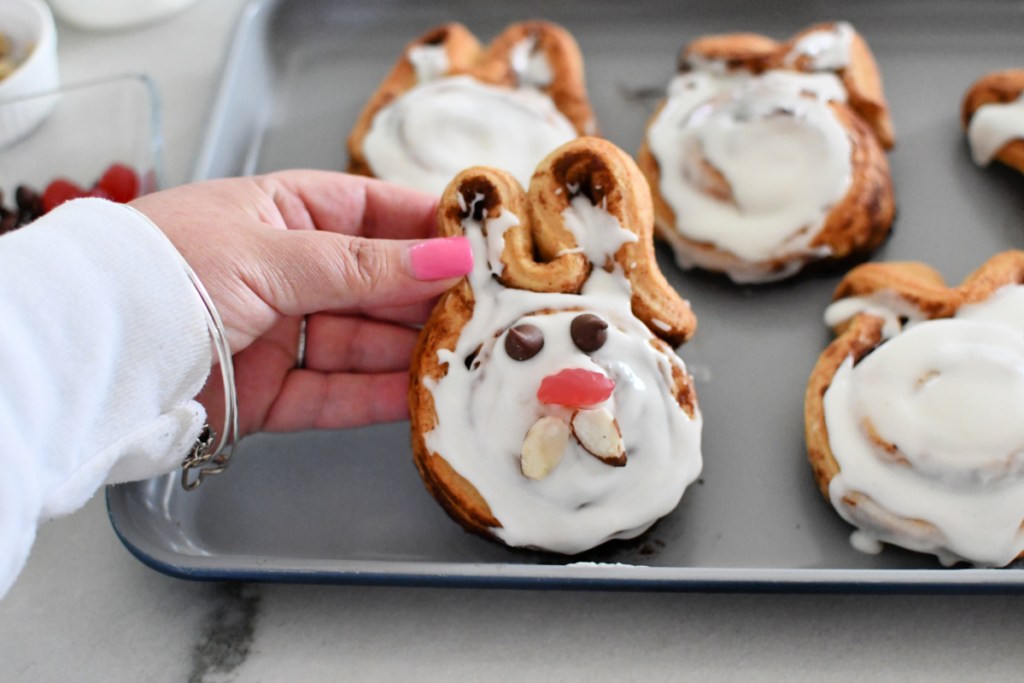 holding an Easter bunny cinnamon roll on a sheet pan