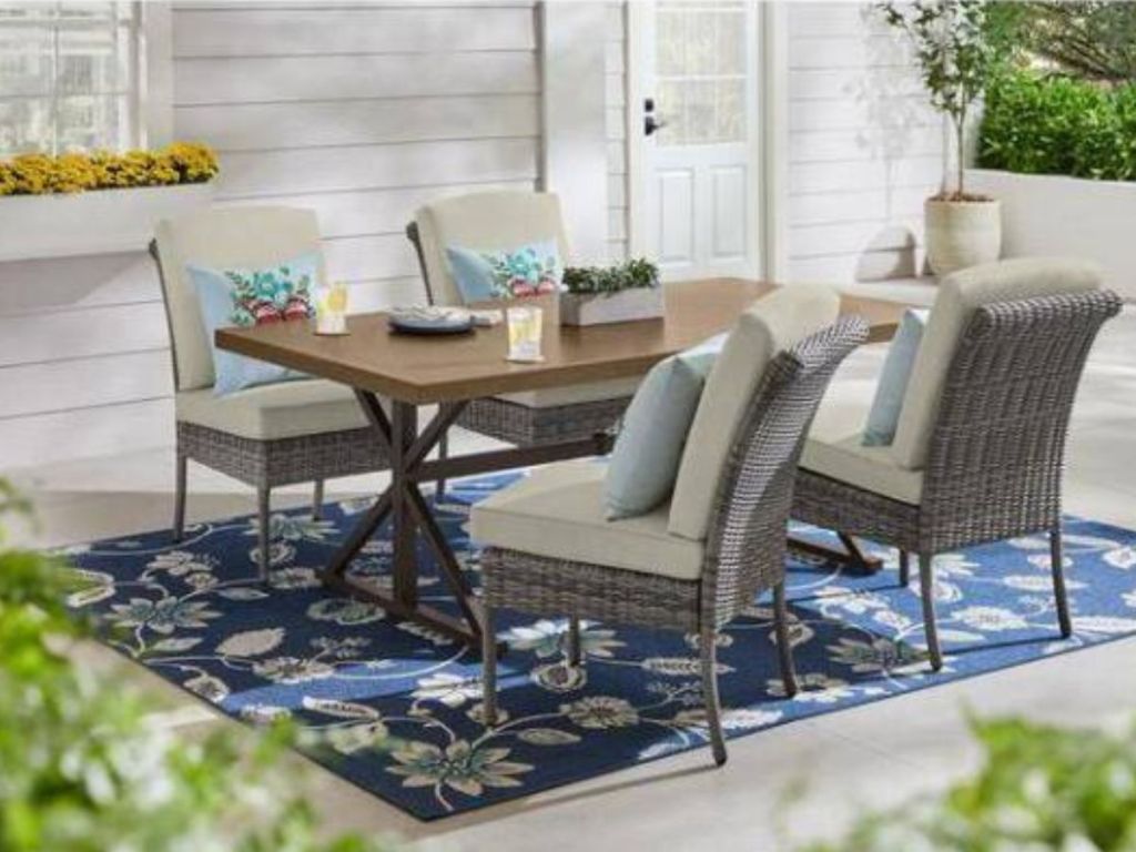 wood table with four wicker chairs with tan cushions dining set on patio