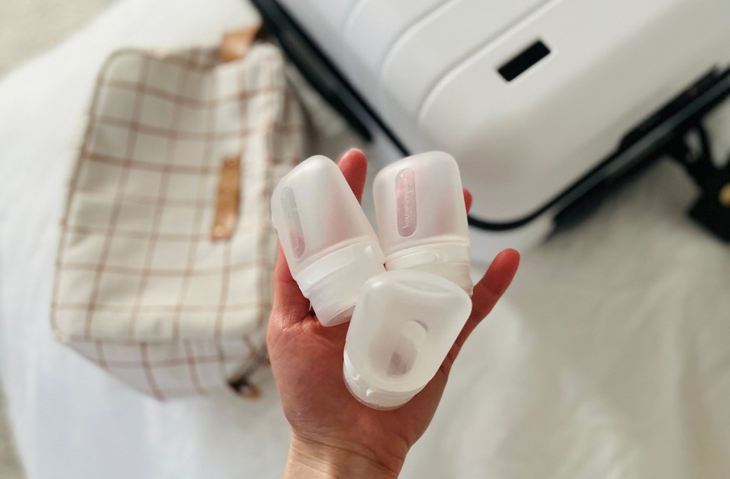 hand holding translucent silicone bottles in hand over white luggage best travel products
