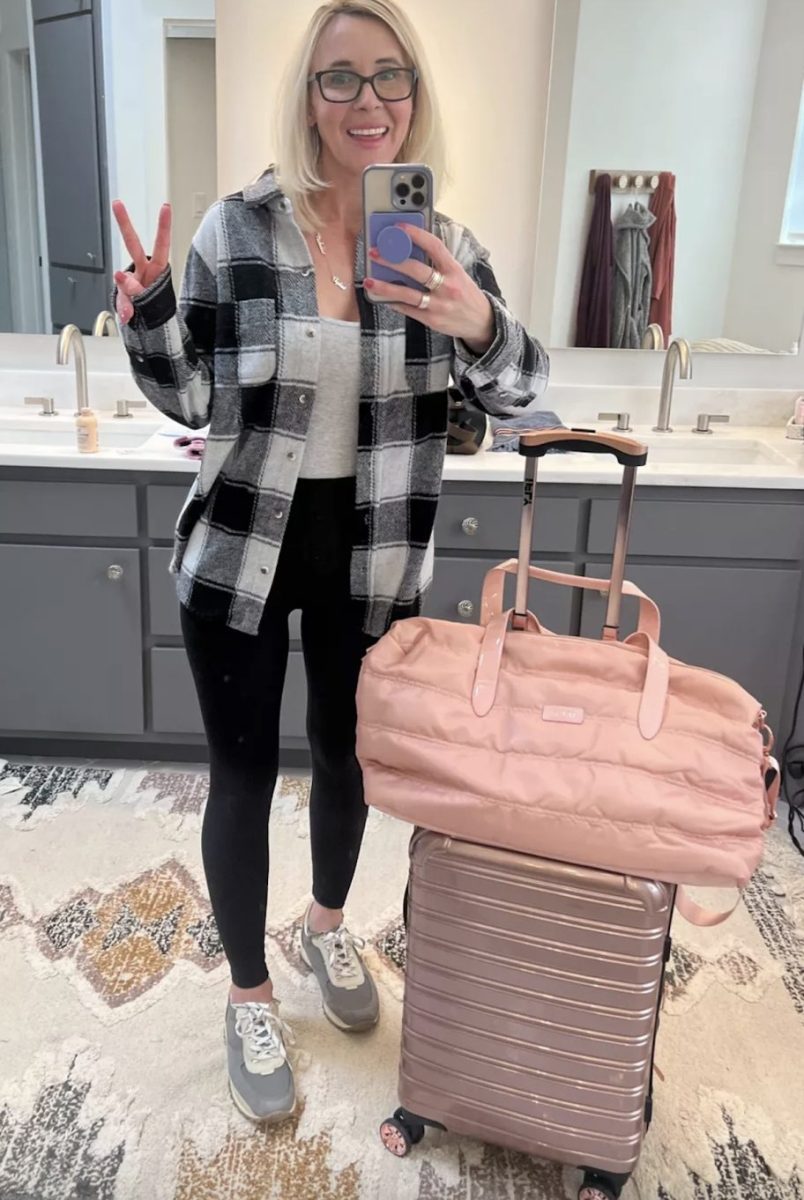 woman holding up peace sign in bathroom mirror next to pink luggage