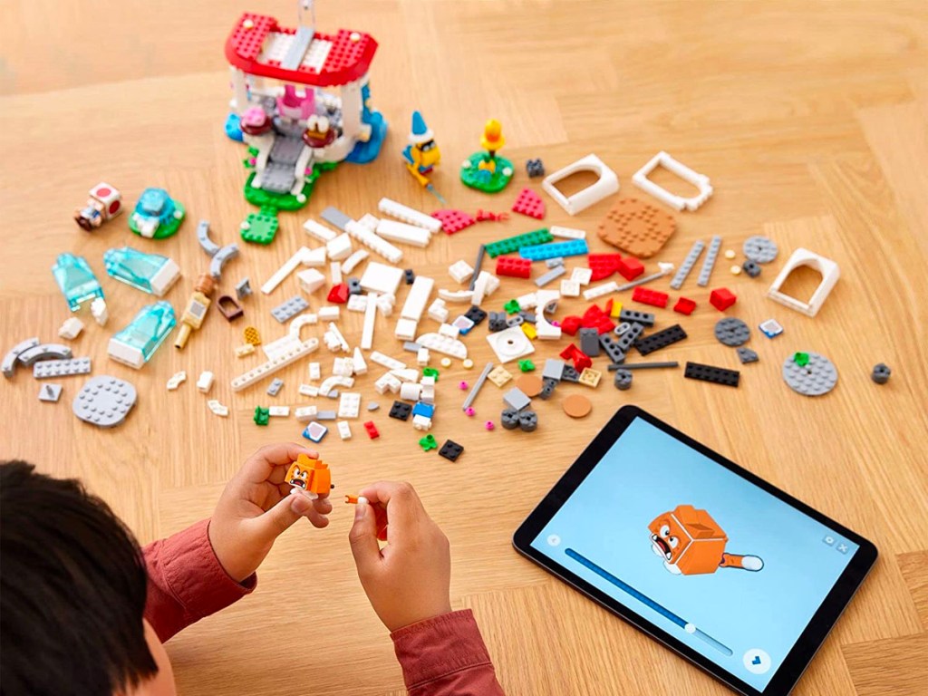 child playing with super mario lego set pieces laid out on table with tablet