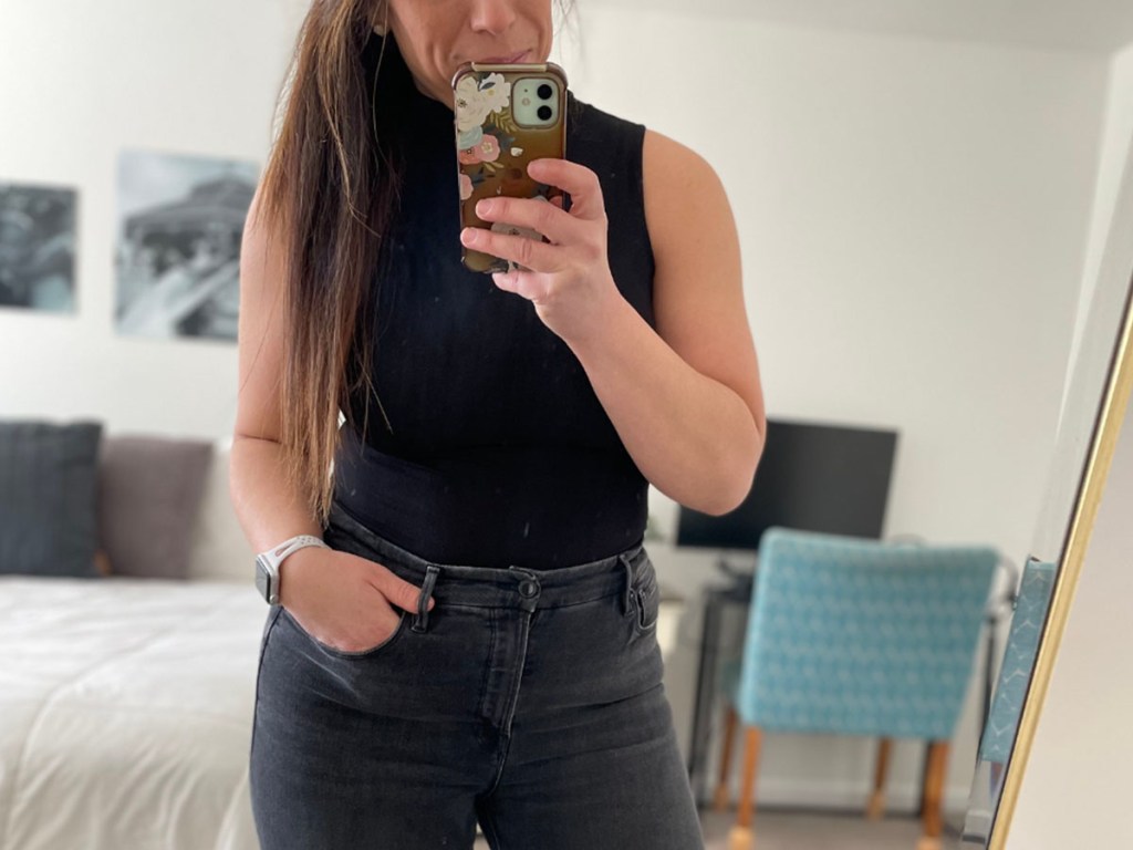 woman taking a mirror selfie in black shirt and jeans