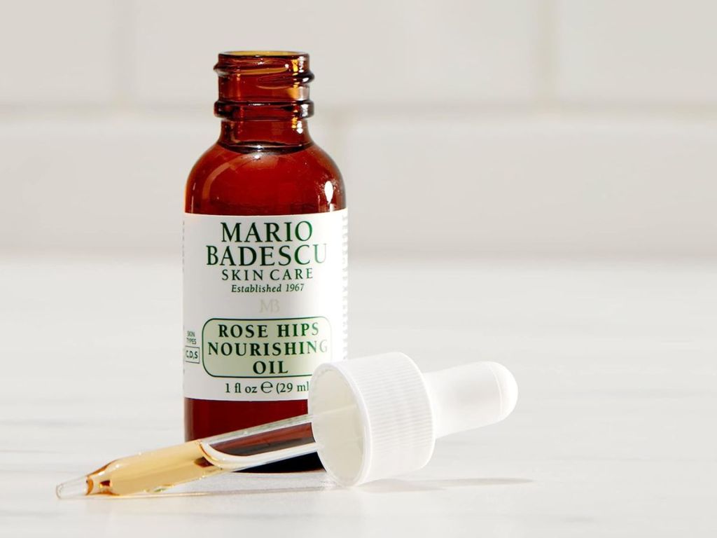 opened bottle of Mario Badescu Rose Hips Oil with dropper half-filled laying next to bottle