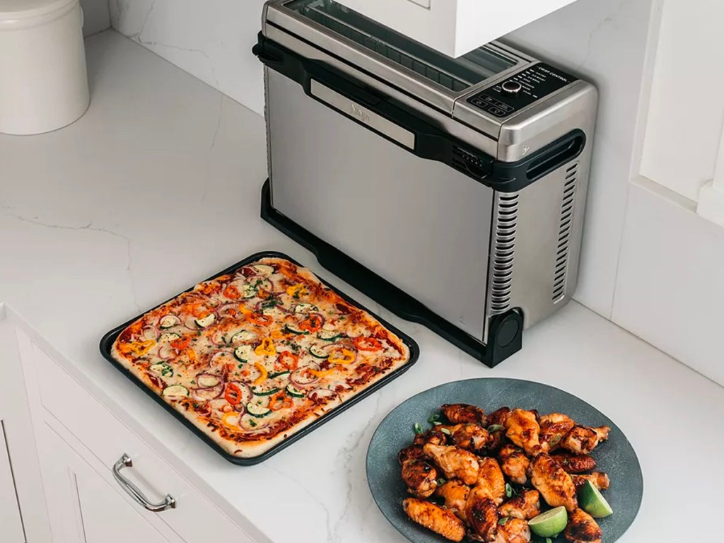 ninja food air fryer standing up with pizza and plate of food