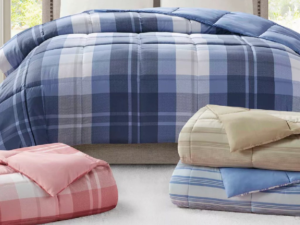 plaid comforter on bed with three more comforters folded on the floor