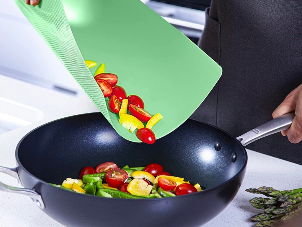 hand pouring veggies off of green cutting board into frying pan