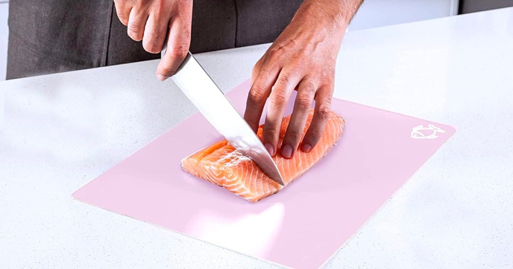 hand cutting fish on pink cutting board