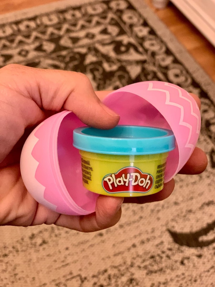 a small can of blue play doh inside a larger pink easter egg being held by a hand