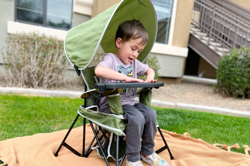 boy sitting in portable high chair with canopy outside