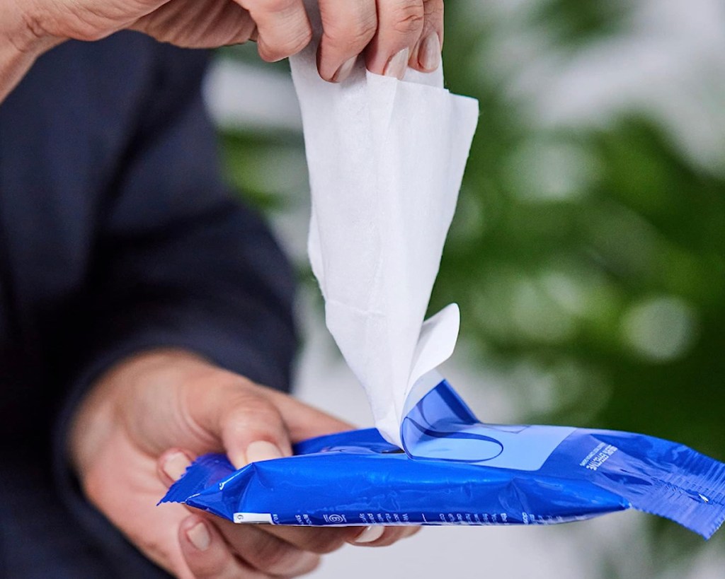 hand pulling out hand sanitizing wipes from travel products package