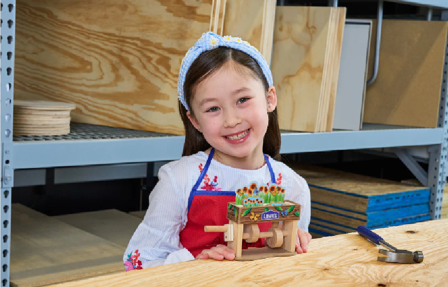 smiling girl building a flower popup box at a lowes kids workshop