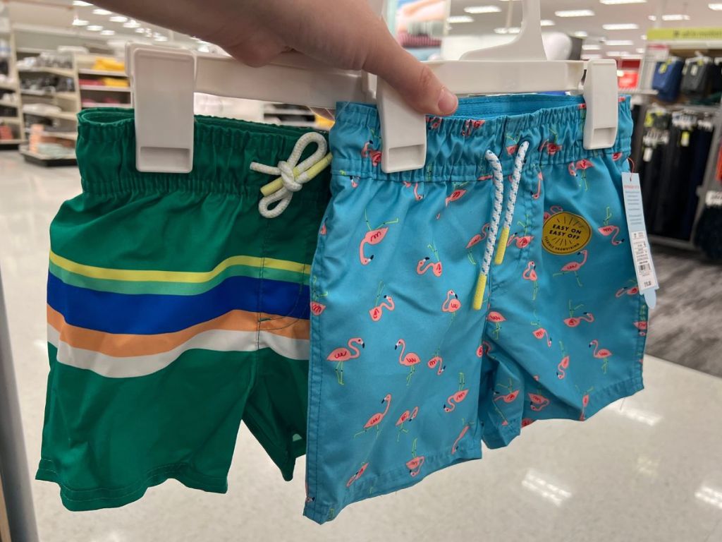 hand holding 2 pairs of boys swim shorts in Target