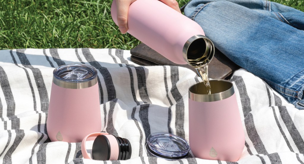 three tumblers in pink laid out on the grass as a picnic