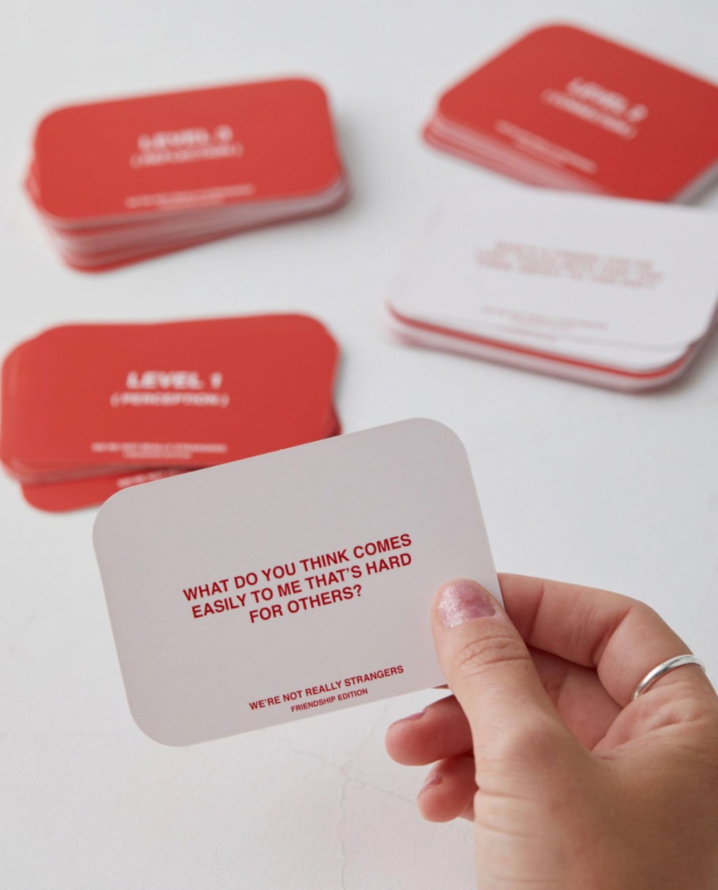 hand holding a red and white question card in front of decks of cards on white table