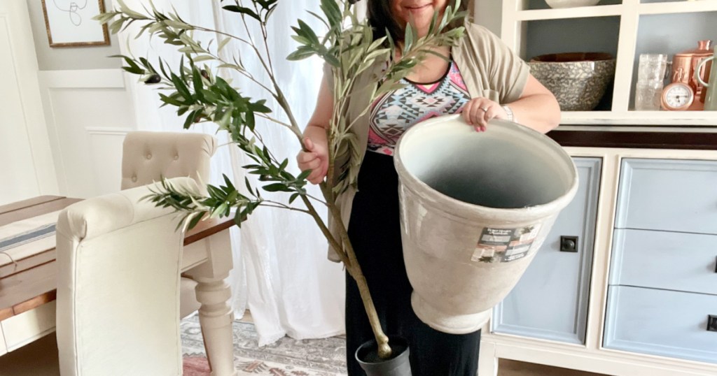 woman holding a faux tree and large planter