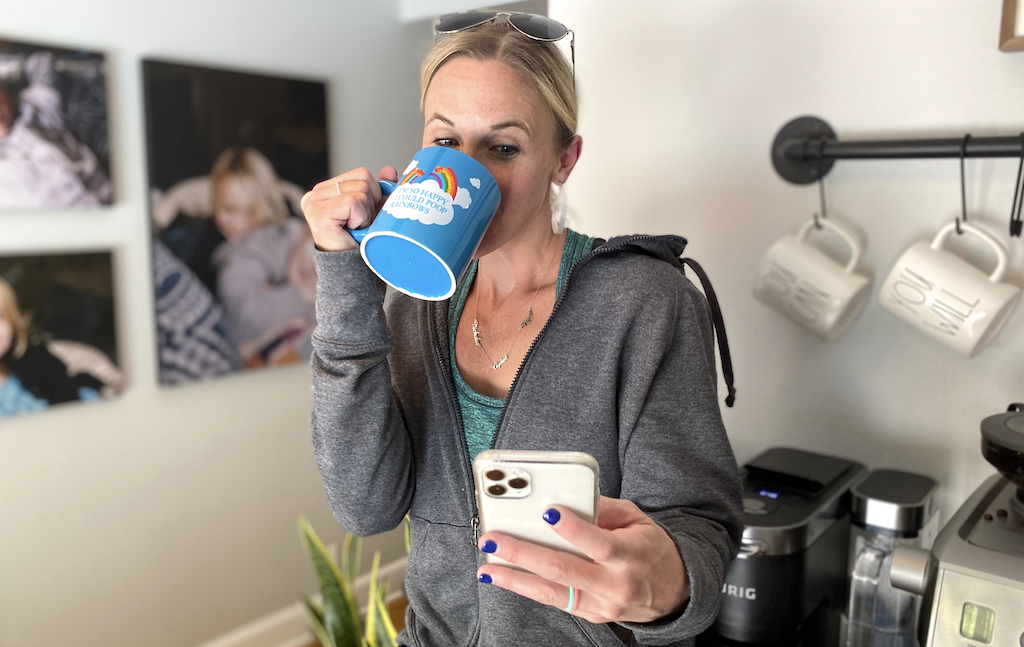 woman drinking coffee and looking at iPhone 