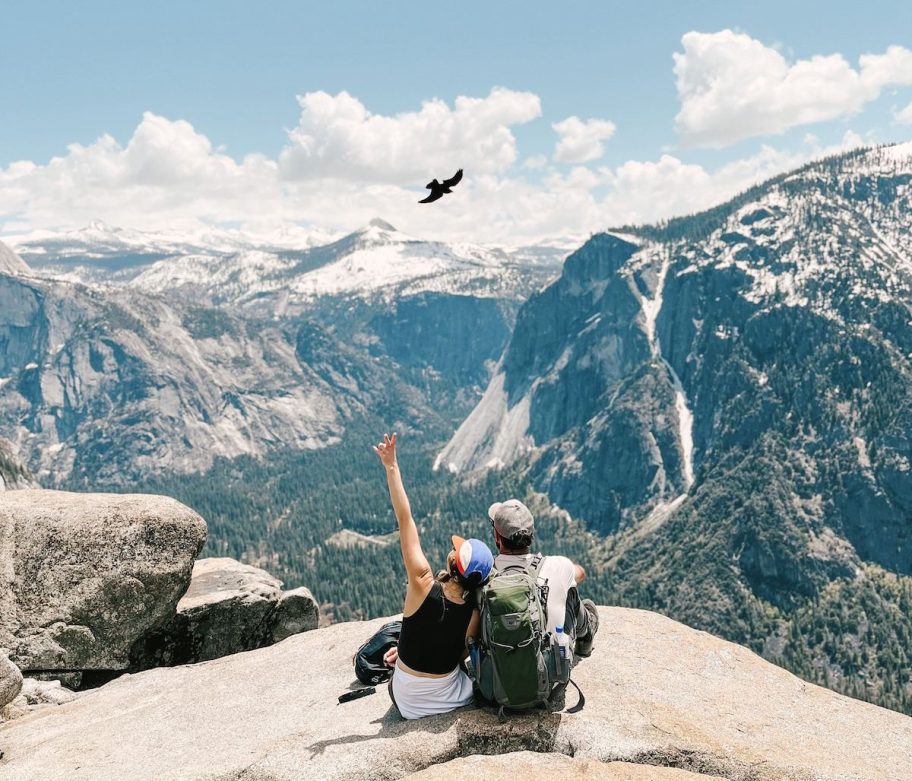 couple sitting on rock at yosemite with bird flying in sky
