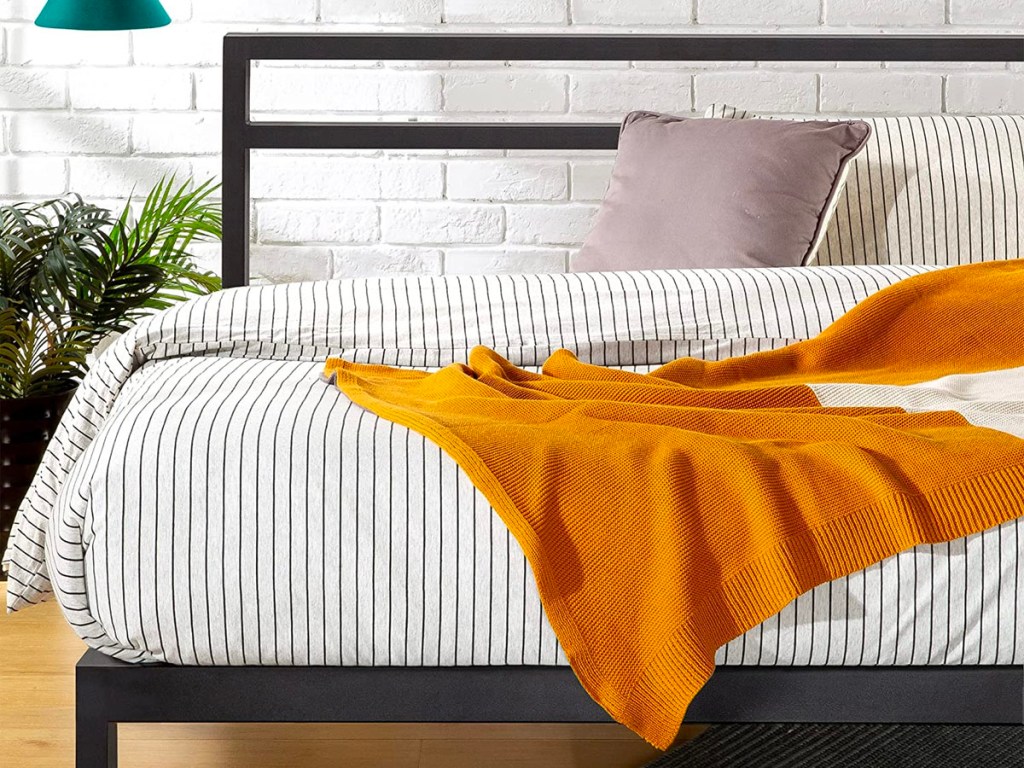 black platform bedframe with striped sheet set and orange blanket