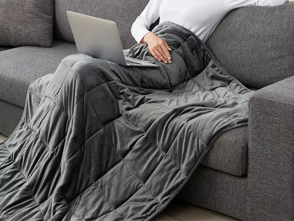 woman sitting on couch under a grey weighted blanket
