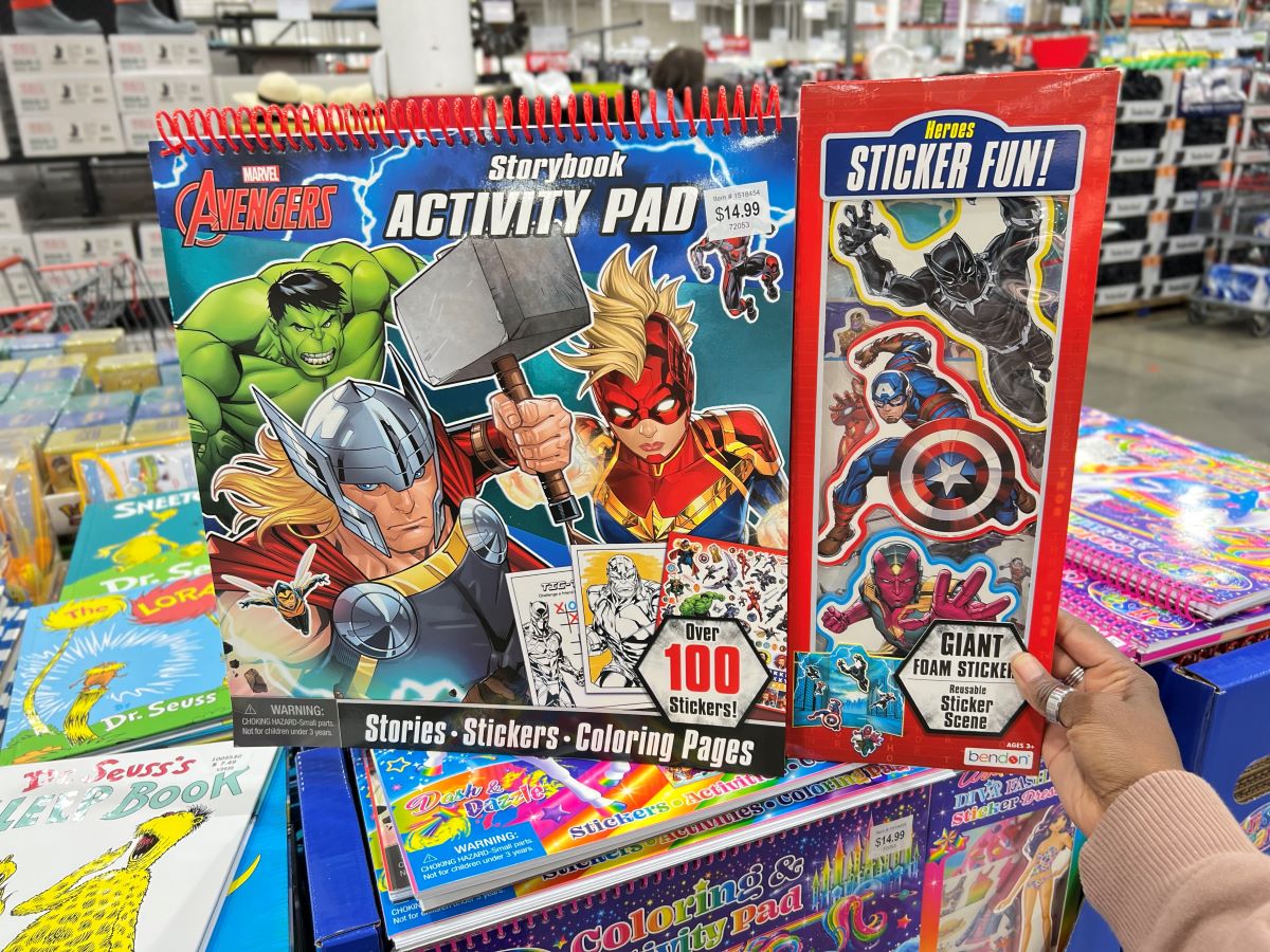 Hand holding a Marvel Avengers Storybook Activity Book on top of other books in store