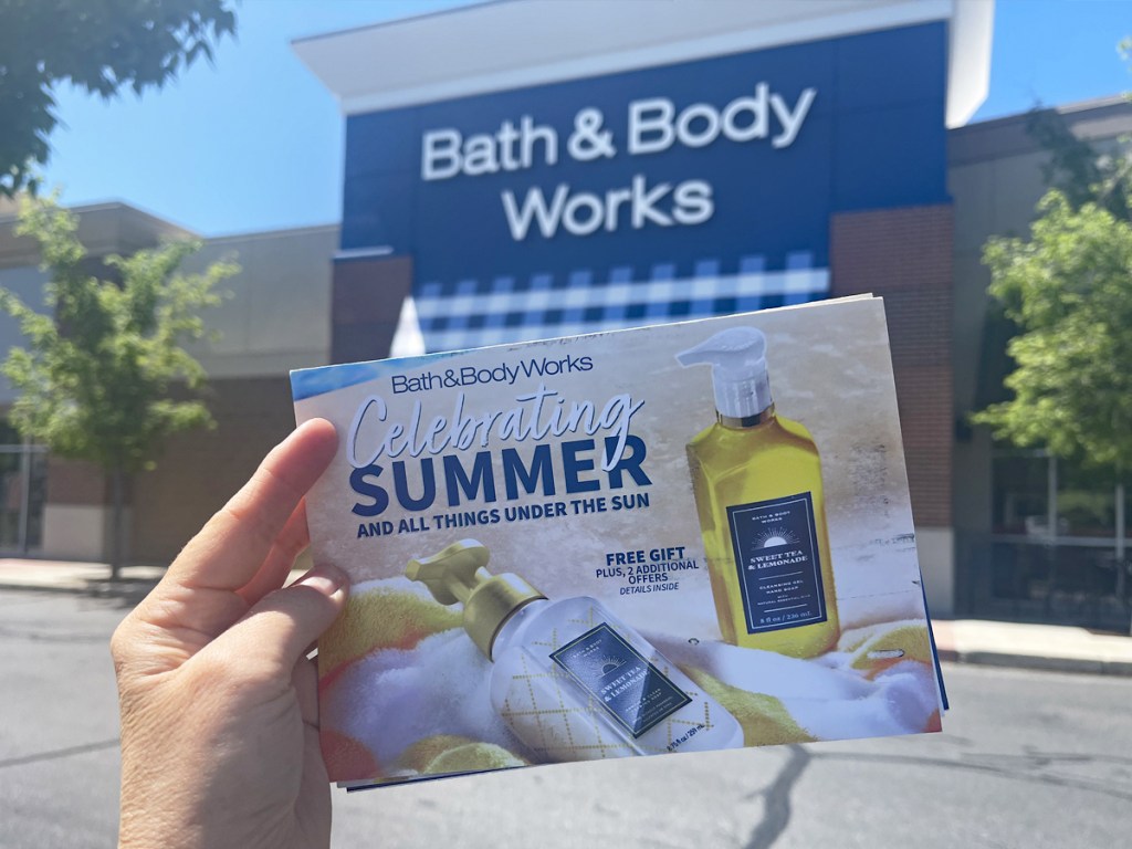 hand holding up Bath & Body Works mailer in front of store