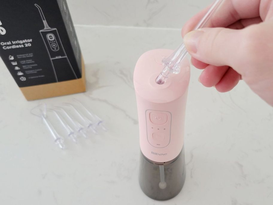 Hand inserting one of the attachments into the top of a pink Bitvae water flosser