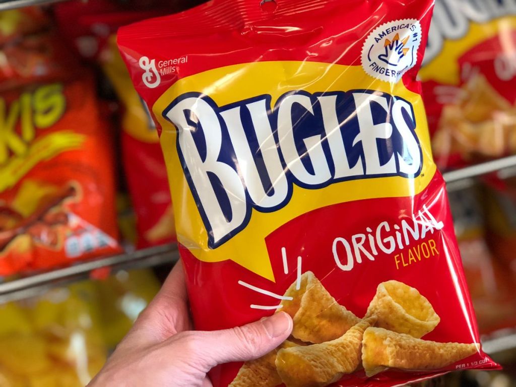 A hand holding a bag of Bugles corn snacks in a store