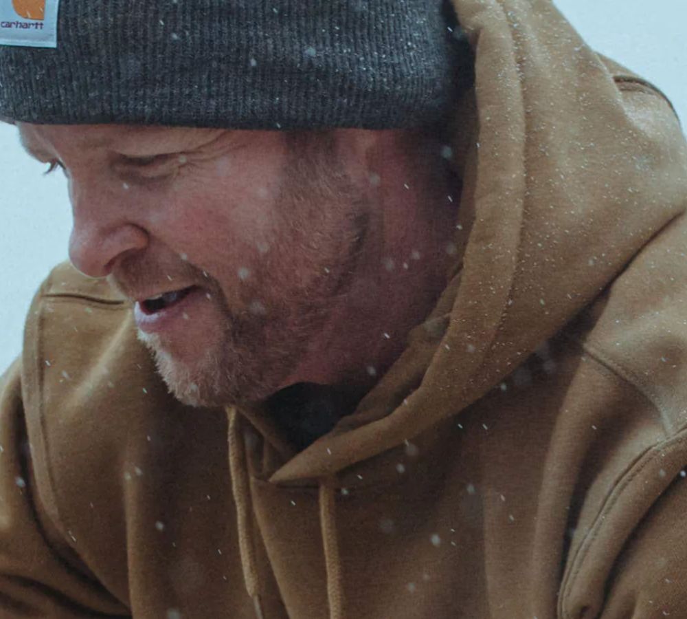 A man wearing a brown hoodie and a gray hat in the snow