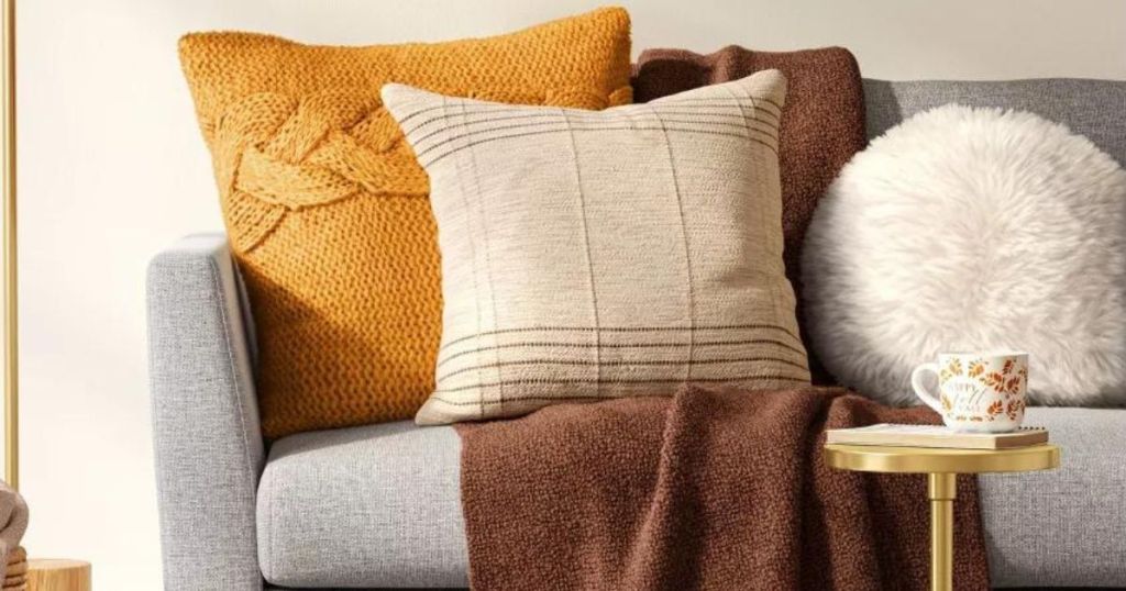 orange and tan throw pillows, brown throw blanket and white round pillow on gray couch