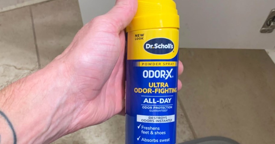 hand holding a yellow and blue can of Dr. Scholl&rsquo;s Odor-X Powder Spray
