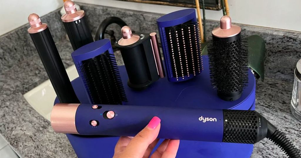 a woman holding a dyson airwrap with the Dyson attachments and case in background